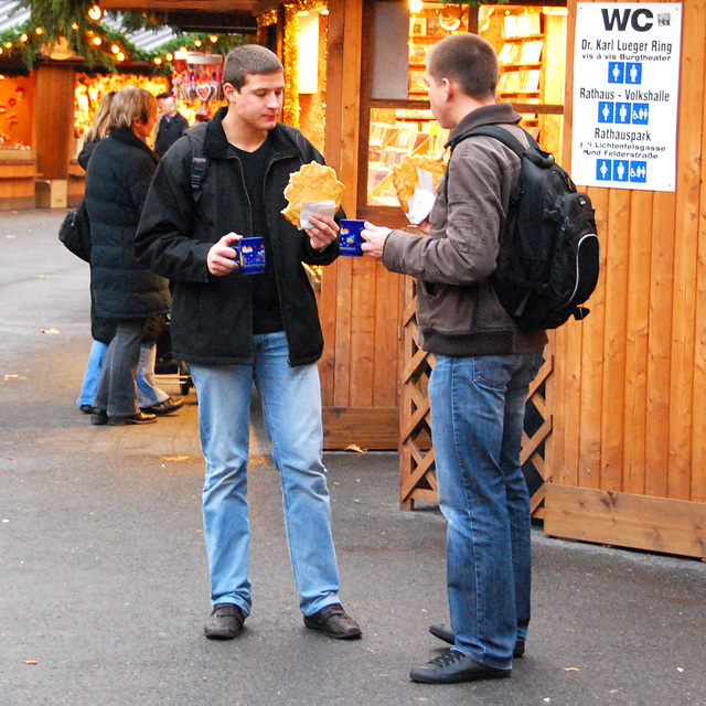 Two young men eating Langos and drinking punsch on the Christmas market