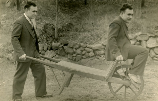 A Man Simultaneously Pushing and Riding a Wheelbarrow