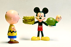 Charlie Brown Looks On in Amazement as Mickey Mouse Poses with Turtle Boy in His Left Hand and a Stack of Pickle Slices in His Right