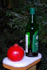 A Pomegranate and bottle of wine on a snow covered fence post.