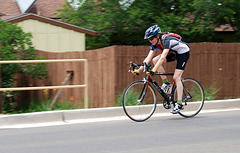 Lady riding a bicycle past a fence.