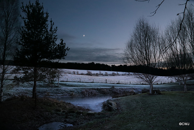 New moon over frosted fields at dusk