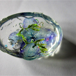 Small oval with blue flower head and greenery