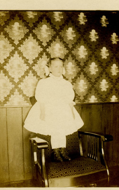 Girl Standing on a Chair in Front of Patterned Wallpaper