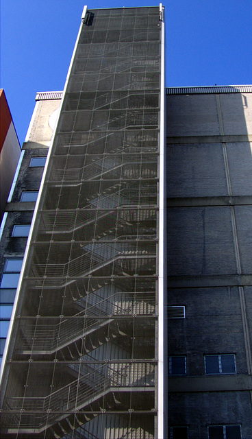 Black stairway in front of grey building with blue sky