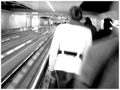 Blurry redhead in white outfit   /   Élégante Dame en blanc sur tapis mécanique -  Brussels airport. - Black & white.