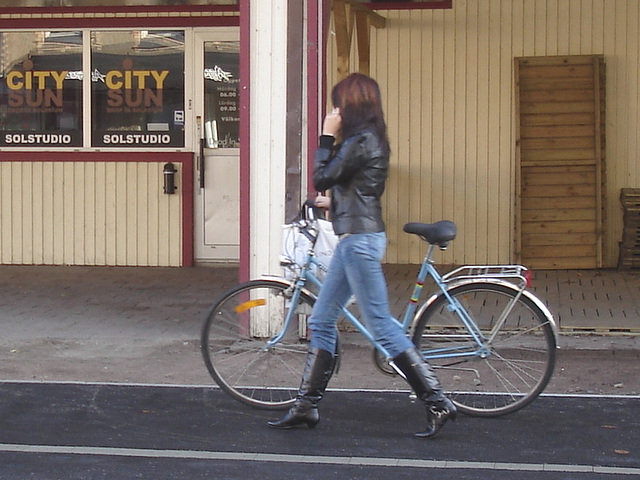 Cycliste en bottes à talons hauts / Walking Swedish biker in jeans & high-heeled boots at her cell phone