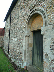 great canfield church,essex,norman north doorway of nave, early c12, with decorated shafts. note smashed remains of stoup to right of door, and original window to left. tympanum is a replacement.