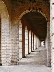 brompton cemetery, earls court,  london,designed in 1838 by benjamin baud, the arcades flanking the central path lead to a circus of similar arcades, with a circular chapel as the point de vue. there are catacombs below some of the arcades.