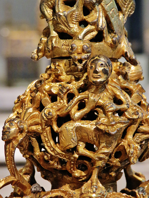 gloucester candlestick, v. and a.,detail of early c12 candlestick with figures and monsters tangled together. this metamorphic figure has a man's upper body which holds a dragon's tail, but his lower 