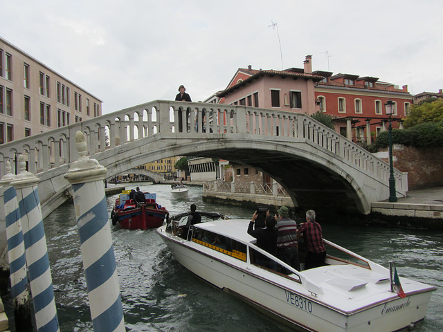 Tourists, getting a very expensive water taxi ride, snap their iPads at the lovely Ventian local on the bridge.