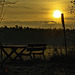 Traffic sign bouncing a tired sun over a hazy scenery. Lonely bench beside. Ennui.