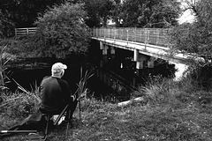 Gentleman fishing by the river crossing footpath, which is protected by a fence!