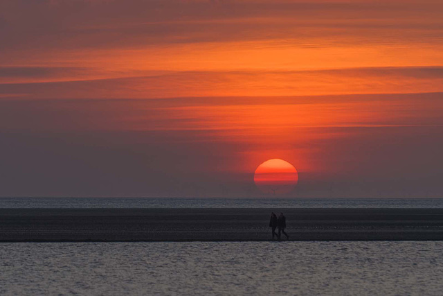 A couple walking in front off the setting sun.