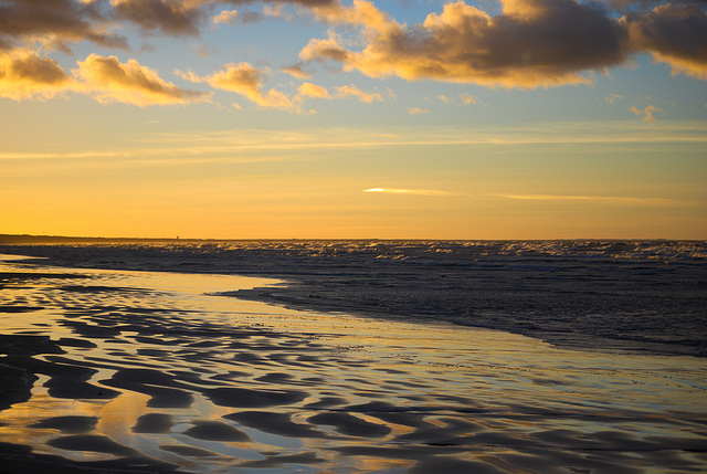 Der nasse Sand und die Wellen beim Sonnenuntergang