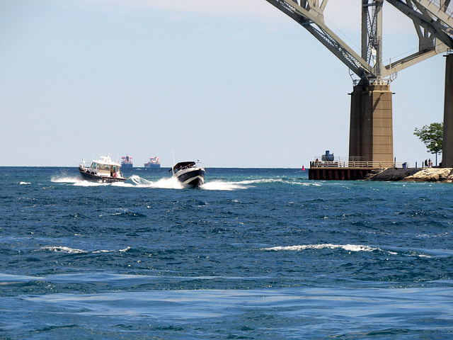 Two freighters anchored in the lake, two boats creating waves.