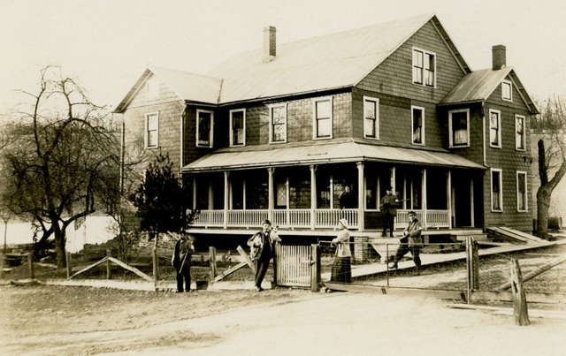 Men, Women, Dogs, and Guns in Front of a House