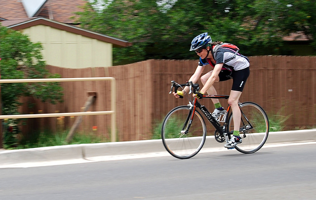 Lady riding a bicycle past a fence.