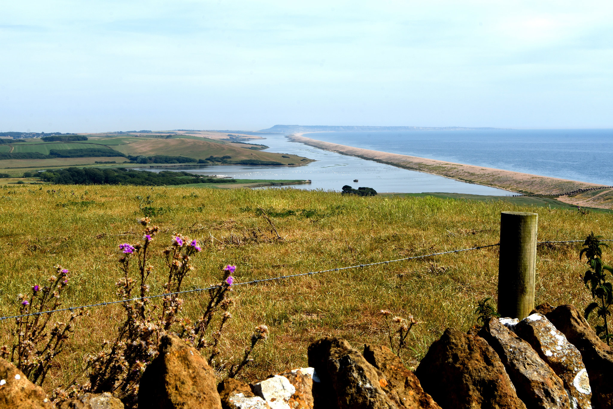 Looking over a barbed wire fence to the Swannery and Chesil beach.