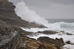A wave breaks over the lower rocks of Pedn Men Du